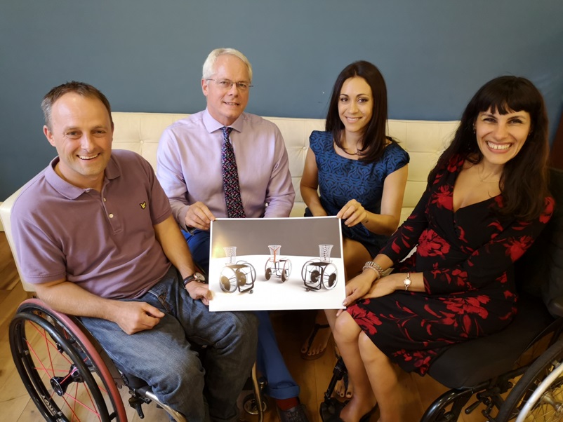Four people holding image of winning competition entry - wheelchair design